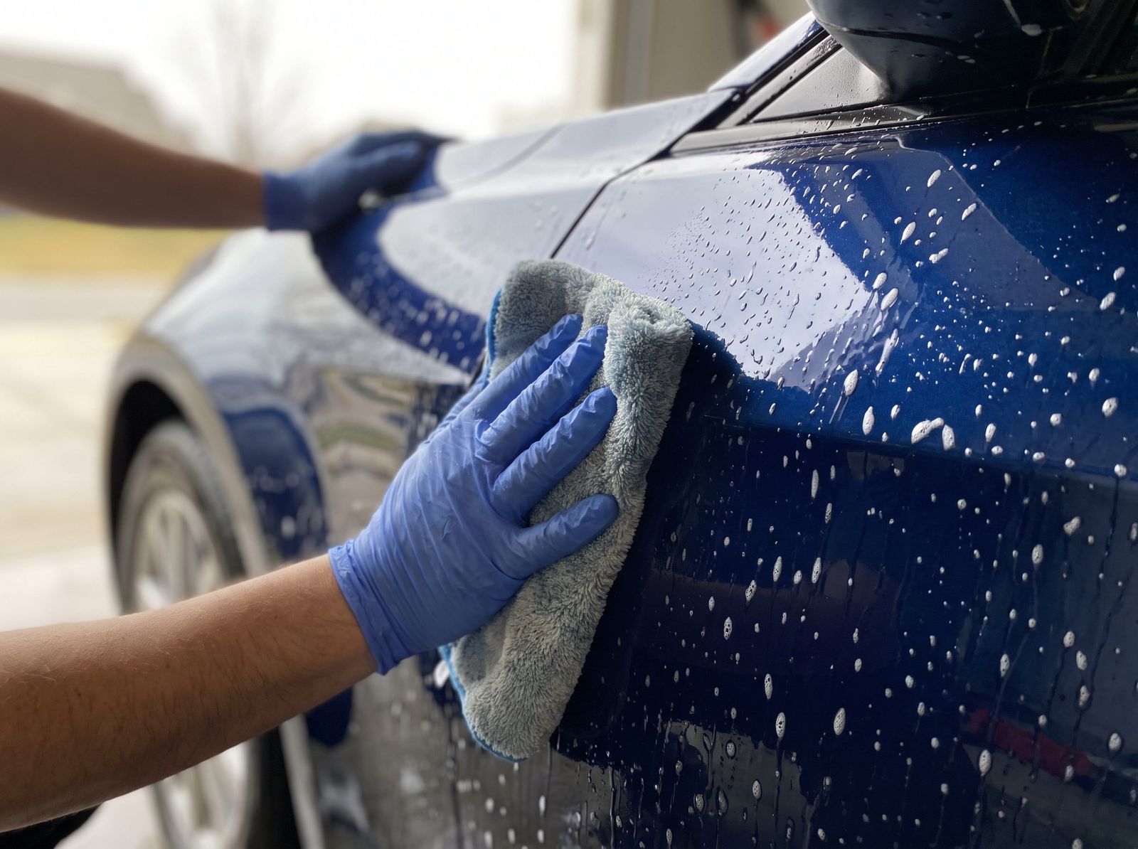 Hands using a microfiber cloth to hand-polish a car exterior during a Discount Detailing service
